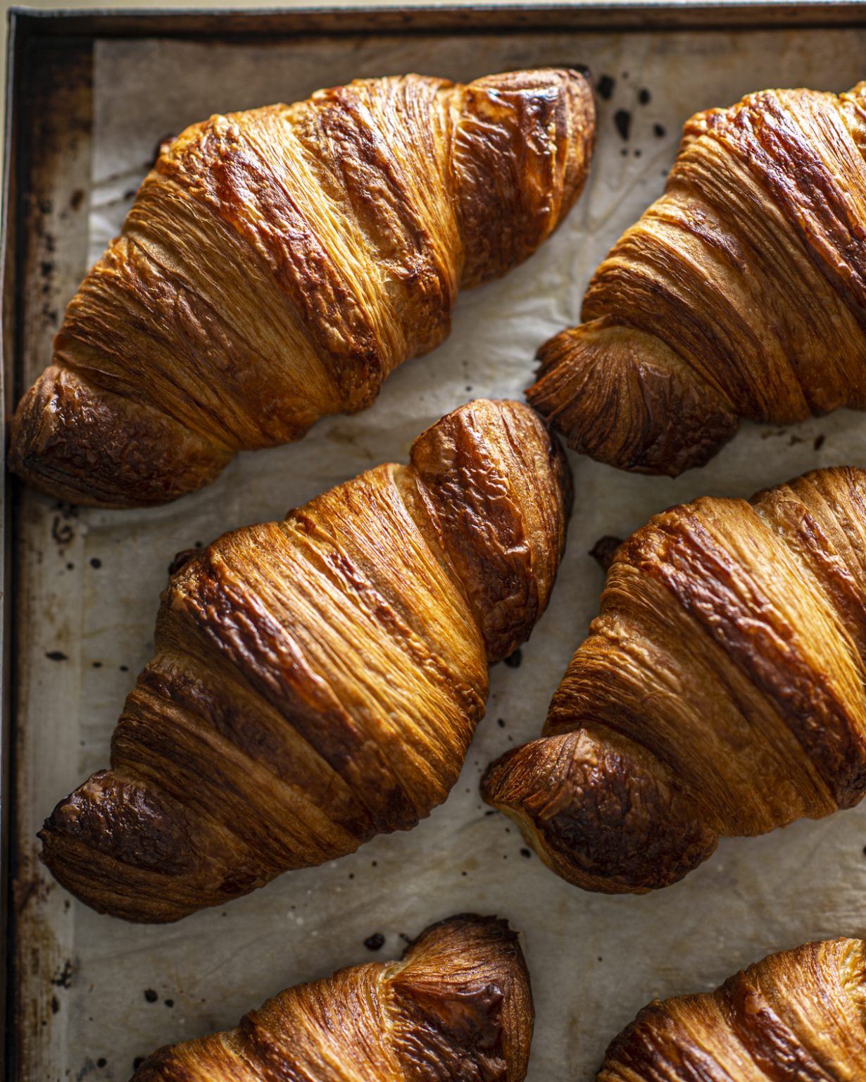 Flaky, golden croissant on a rustic surface, freshly baked and buttery.